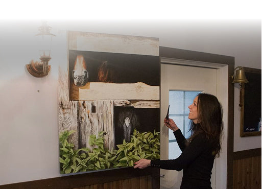 Siret Põllu hunging up a large unframed artwork of a horses in a room with a white wall and door.