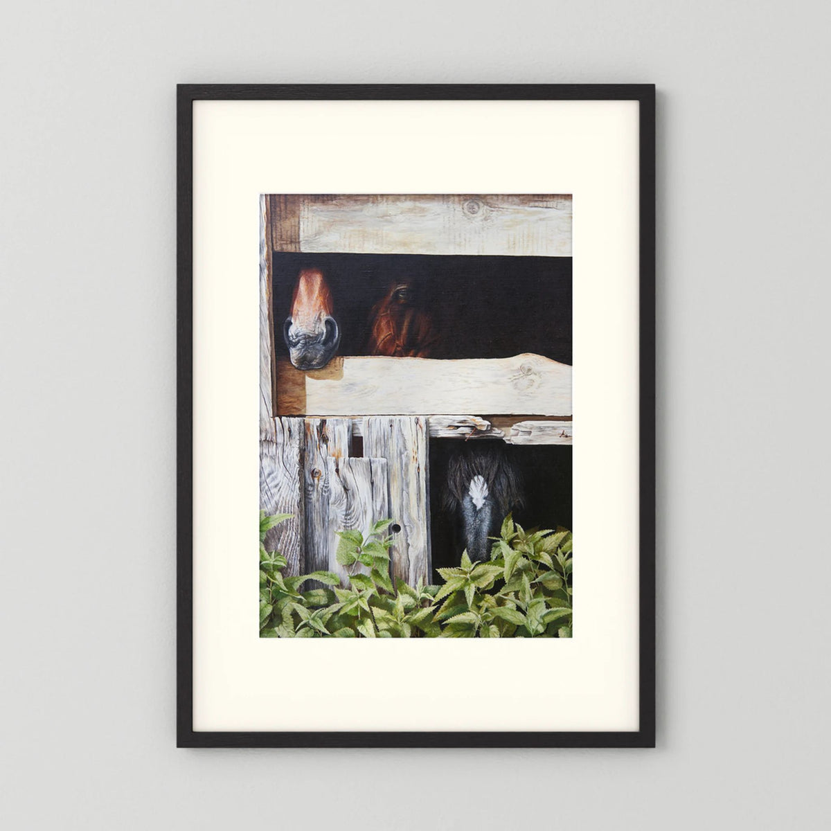 A framed (black frame) paper art print with a freja passepartout featuring a rustic barn scene with horses peeking out from wooden stalls, displayed against a light gray wall.