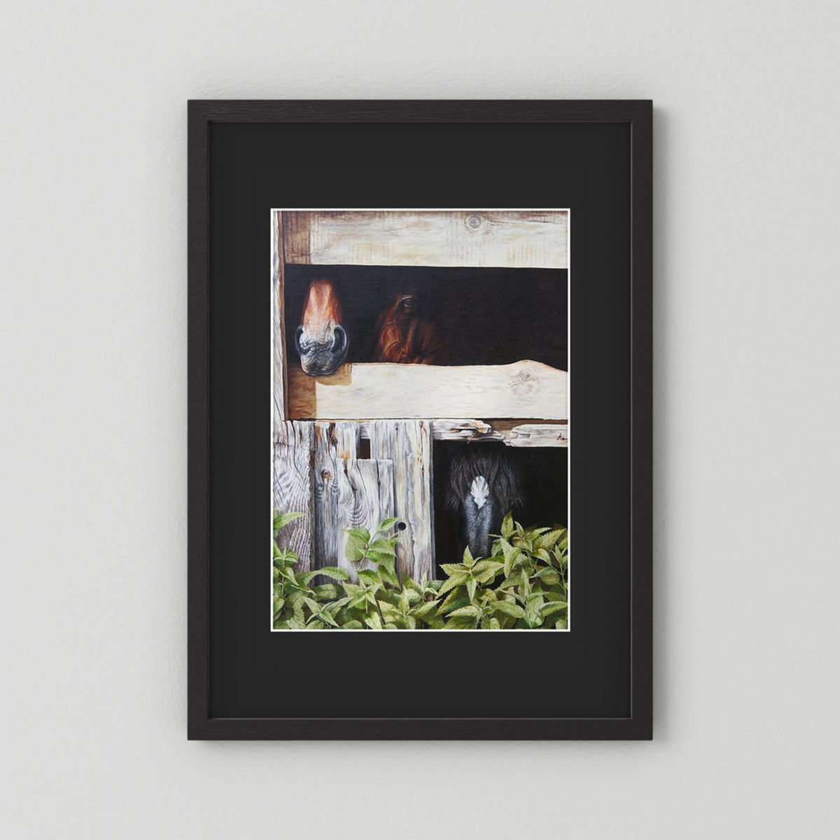 A framed (black frame) paper art print with a black passepartout of three horses in a stable, presented against a light gray wall.
