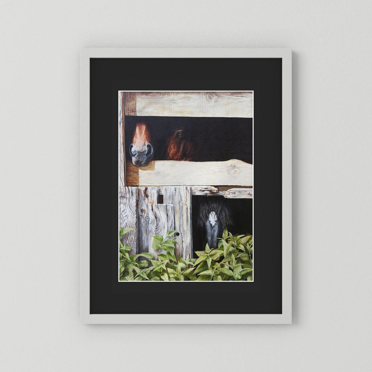 Framed (white frame) paper art print with a black passepartout featuring a painted scene of three horses peeking out from wooden stalls, displayed on a light gray wall.