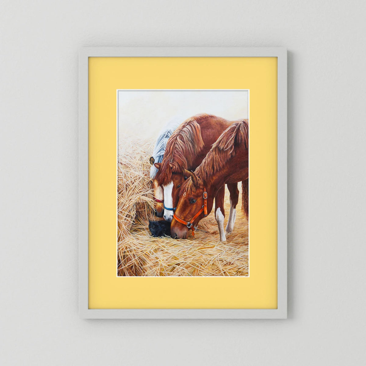 A framed (white frame) paper art print with a yellow passepartout featuring a painting of three young horses and a black cat displayed against a neutral light gray background.